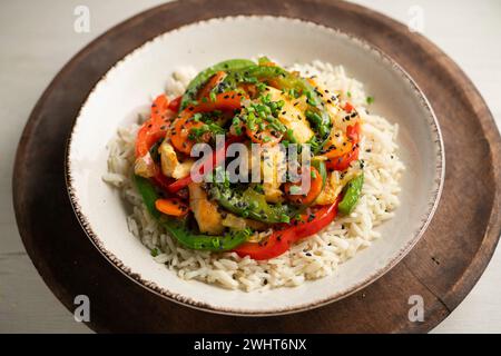 Poulet cuit dans un wok avec des poivrons colorés et du riz. Banque D'Images