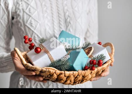Femme tenant panier avec des cadeaux de Noël emballés durables, gros plan, focus sélectif. Décoration de Noël écologique Banque D'Images