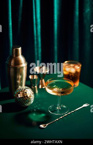 Champagne en verre, shaker, cuillère de mélange cocktail et jigger sur table vert foncé Banque D'Images