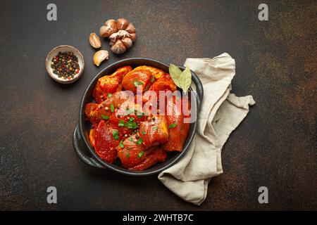 Morceaux de viande hachés crus non cuits marinés avec des assaisonnements et du persil dans une casserole noire vue de dessus sur dos rustique foncé Banque D'Images