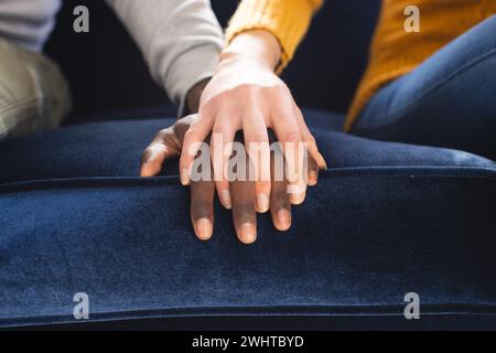 Section médiane de divers couples assis sur un canapé tenant les mains à la maison Banque D'Images