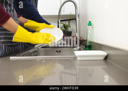 Section médiane de divers couples faisant la vaisselle dans la cuisine à la maison Banque D'Images