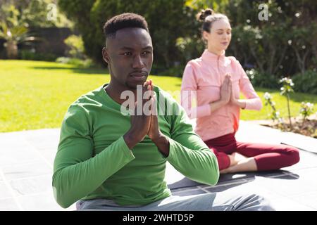 Couple diversifié pratiquant le yoga et méditant dans le jardin Banque D'Images