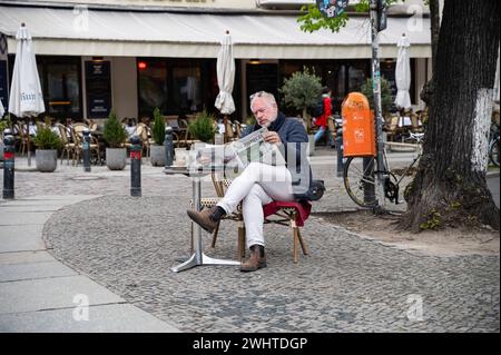 02.05.2023, Berlin, Deutschland, Europa - Ein Mann sitzt auf einem Stuhl unweit eines Strassencafes am Savignyplatz im Berliner Bezirk Charlottenburg-Wilmersdorf und Most eine Tageszeitung. *** 02 05 2023, Berlin, Allemagne, Europe Un homme est assis sur une chaise non loin d'un café de rue sur Savignyplatz dans le quartier Berlins Charlottenburg Wilmersdorf et lit un journal quotidien Banque D'Images