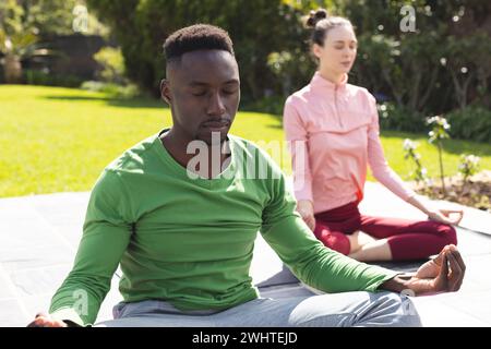 Couple diversifié pratiquant le yoga et méditant dans le jardin Banque D'Images