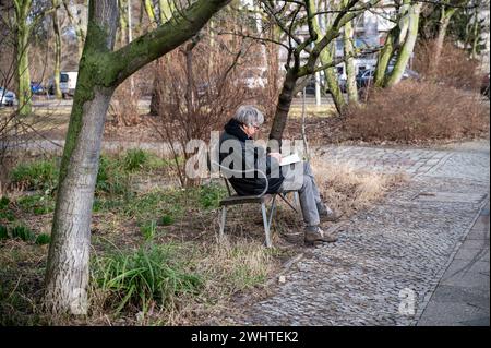 10.02.2024, Berlin, Allemagne, Europe - un homme âgé est assis sur un banc au bord de la route lisant un livre dans la localité berlinoise de Tiergarten. Banque D'Images