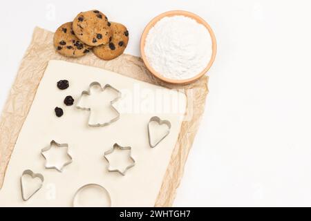 Pâte pour cuire des biscuits sur papier. Moules pour emporte-pièces. Farine dans un bol et biscuits prêts à l'emploi. Copier l'espace. Pose à plat. Fond blanc. Banque D'Images