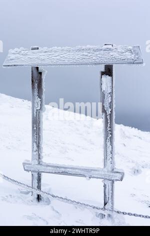 Poste d'information en bois vide sur le sentier d'hiver. Photo prise pendant une journée neigeuse et nuageuse. Banque D'Images