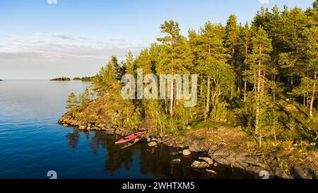 Des kayaks touristiques se tiennent au bord de la côte rocheuse pittoresque avec une forêt de pins. Une île magnifique dans un grand lac lors d'une chaude soirée d'été. Vue aérienne. Banque D'Images