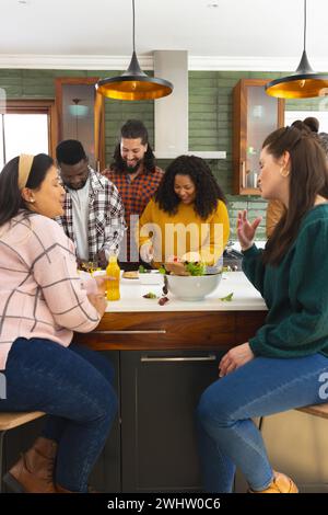 Heureux divers amis masculins et féminins préparant le repas et buvant des boissons dans la cuisine Banque D'Images