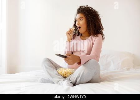 Contenu du choc. Femme enceinte noire regardant la télévision et mangeant du Popcorn à la maison Banque D'Images