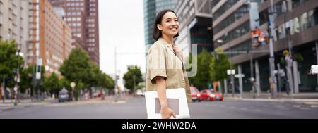 Photo extérieure d'une fille asiatique avec un ordinateur portable, aller quelque part dans le centre-ville, marcher dans la rue, aller au travail Banque D'Images