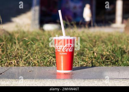 Biélorussie, Minsk - 29 octobre 2023 : verre de Coca Cola sur trottoir près de l'herbe Banque D'Images