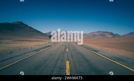 Une route asphaltée mène à travers le désert d'Atacama au Chili le long de paysages de sable rouge, d'énormes volcans et de montagnes enneigées. Banque D'Images