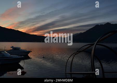 Beau coucher de soleil rouge avec des bateaux à moteur ancrés à la jetée du lac et un détail de bateau de pêche en bois traditionnel italien du lac de Côme 'Lucia'. Grand ciel sombre. Banque D'Images