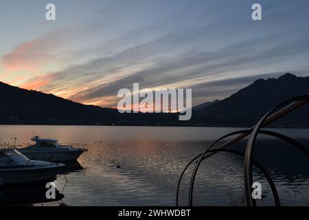 Beau coucher de soleil rouge avec des bateaux à moteur ancrés à la jetée du lac et un détail de bateau de pêche en bois traditionnel italien du lac de Côme 'Lucia'. Grand ciel sombre. Banque D'Images