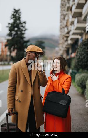 Un élégant couple d'affaires multiracial dans la tenue à la mode engagé dans une conversation animée tout en marchant dans la rue par une journée couverte. Banque D'Images