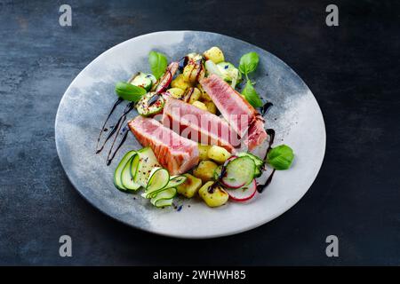 Steak de thon frit italien traditionnel avec gnocchi et tranches de concombre servi en gros plan sur une assiette au design nordique Banque D'Images