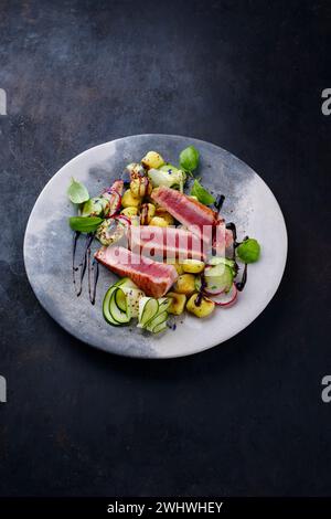 Steak de thon frit italien traditionnel avec gnocchi et tranches de concombre servi en gros plan sur une assiette au design nordique Banque D'Images