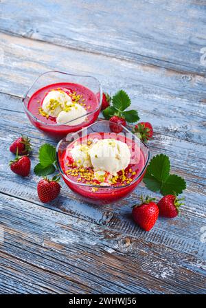 Soupe traditionnelle aux fraises congelée avec glace à la vanille et pistaches écrasées servis en gros plan sur une planche de bois rustique w Banque D'Images