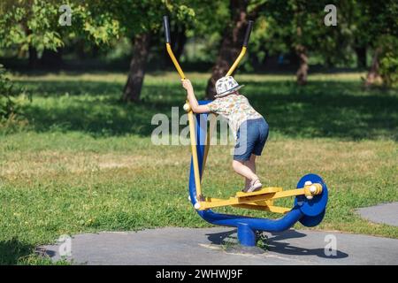 Petit garçon sur la machine d'entraînement de ski adulte dans le parc de la ville. Banque D'Images