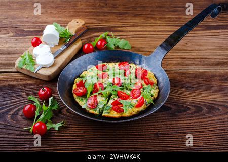 Omelette végétarienne traditionnelle allemande à la rucola avec tomates cerises et fromage de chèvre à la crème servie en gros plan dans un fryi en fer forgé Banque D'Images