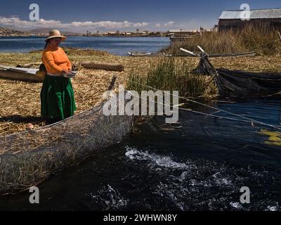 Femme andine en costume typique nourrissant des poissons sur les îles Uros dans le lac Titicaca, Puno, Pérou. Banque D'Images