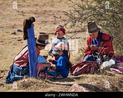 Famille autochtone péruvienne assis à la campagne avec des enfants et des robes typiques avec des fils pour le tissu, Moray, Cuzco, Pérou Banque D'Images