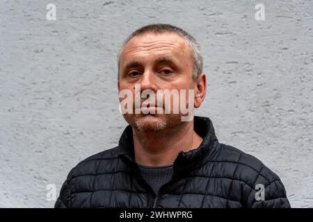 Un homme âgé aux cheveux gris de 45-50 ans, contre un mur de couleur claire portant une veste noire, regarde la caméra. Banque D'Images