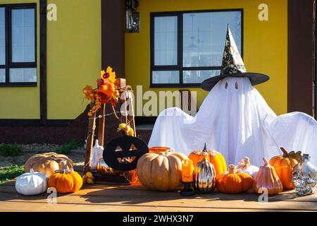 Enfant dans le drap de lit avec des fentes comme fantôme dans le chapeau de sorcière et le décor d'Halloween sur le porche de la maison à l'extérieur dans la cour de pum Banque D'Images