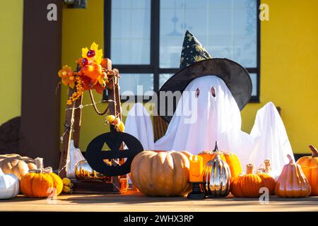 Enfant dans le drap de lit avec des fentes comme fantôme dans le chapeau de sorcière et le décor d'Halloween sur le porche de la maison à l'extérieur dans la cour de pum Banque D'Images