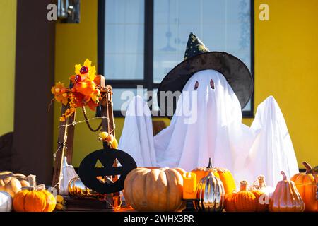 Enfant dans le drap de lit avec des fentes comme fantôme dans le chapeau de sorcière et le décor d'Halloween sur le porche de la maison à l'extérieur dans la cour de pum Banque D'Images