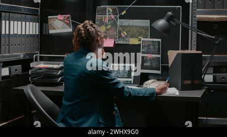 Agent de police prenant des notes sur les dossiers de cas dans la salle d'incident, essayant de résoudre l'activité criminelle et d'attraper le suspect. Inspecteur professionnel examinant les photos de recherche et de surveillance. Banque D'Images