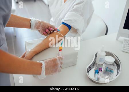 Jeune femme brune dans un manteau blanc fait des procédures médicales. Une infirmière en gants et en vêtements médicaux prend du sang Banque D'Images