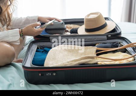 Femme emballant valise sur le lit pour une nouvelle liste d'emballage de voyage pour la planification de voyage préparer des vacances Réservez maintenant Voyage transport Banque D'Images