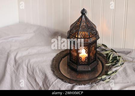 Lanterne arabe marocaine noire brûlante avec plateau en argent, brindilles d'olivier sur la table avec nappe de lin. Fond de mur en bois blanc. Fête musulmane Banque D'Images