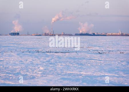 Fumée des tuyaux de la ville à l'horizon et un paysage urbain de champ enneigé Banque D'Images