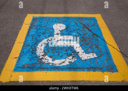 Peint en bleu et blanc avec un pictogramme de stationnement pour handicapés à cadre jaune sur la surface asphaltée du stationnement. Banque D'Images