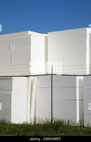 Piles de panneaux de polystyrène blanc derrière la clôture de sécurité en treillis métallique dans la cour de stockage extérieure. Banque D'Images