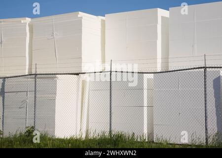 Piles de panneaux de polystyrène blanc derrière la clôture de sécurité en treillis métallique dans la cour de stockage extérieure. Banque D'Images