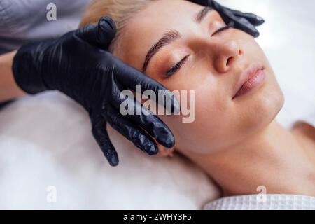 Gros plan d'un maître appliquant des patchs en silicone sous les yeux d'une jolie cliente blonde féminine Banque D'Images