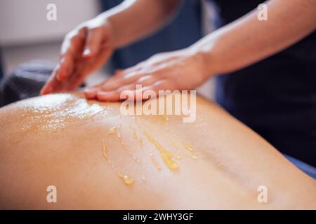 Massage de la zone du collier cervical avec du miel. La cliente est allongée sur la table et reçoit un massage du dos dans un salon de spa ou clin Banque D'Images