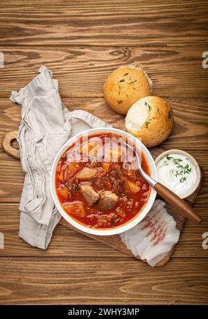 Borscht ukrainien, soupe de betteraves rouges à la viande, dans un bol blanc avec crème sure, petits pains à l'ail Pampushka et tranches de salo, sto rustique Banque D'Images