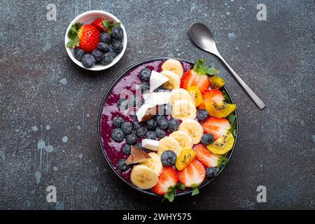 Bol de smoothie d'acai d'été sain avec des graines de chia, banane fraîche, fraise, myrtille, cocos, kiwi vue de dessus, béton rustique ba Banque D'Images