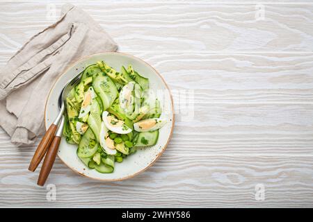 Saladier d'avocat vert sain avec œufs durs, concombres tranchés, haricots edamame, huile d'olive et herbes sur le dessus de la plaque en céramique vie Banque D'Images