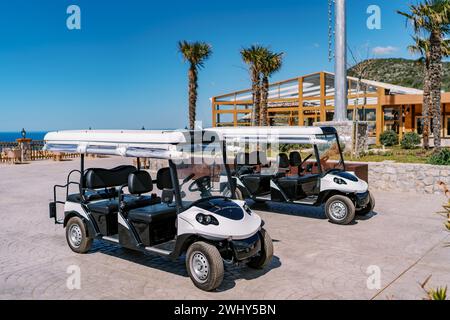 Des voiturettes de golf blanches se trouvent dans un parking carrelé en face de l'hôtel, au milieu des palmiers Banque D'Images