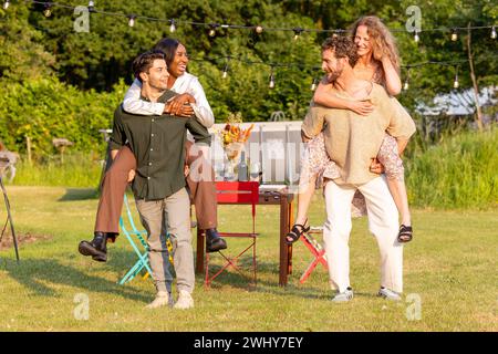 Amis milléniaux multi ethniques engagés dans la course de piggyback amusante à Garden Party Banque D'Images
