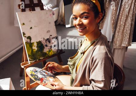 Jeune femme créative jolie artiste afro-américaine peint l'image avec des peintures à l'huile dans le studio d'art. Banque D'Images