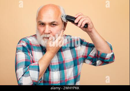 Portrait d'un homme âgé en train d'être tondu avec une tondeuse électrique professionnelle dans un salon de coiffure, coupe de cheveux avec un rasoir électrique. Banque D'Images