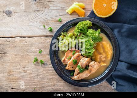 Filet de poulet frit à la sauce orange avec brocoli et légumes de poireau sur une assiette bleu foncé et serviette sur une table en bois rustique, Banque D'Images